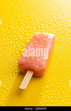 Fruity ice lolly. Sweet popsicle on yellow table with a water drops. Stock Photo