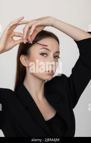 Vertical woman face look at camera trimming and correcting, brushing eyebrows by brush, checking brow eye line. Closeup Stock Photo