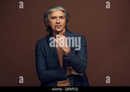 Portrait of cheerful satisfied mature businessman in jacket reaching hand for handshaking, brown background Stock Photo