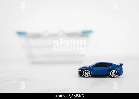 toy car inside of shopping basket over white marble background, concept of buying a new car Stock Photo