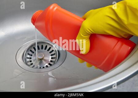 Hand in yellow rubber glove pour sewer pipe cleaner down the kitchen sink drain. Kitchen and drain cleaning work Stock Photo