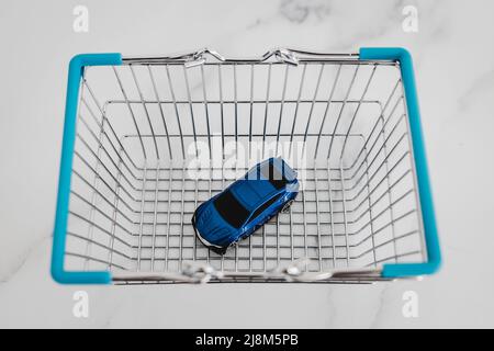 toy car inside of shopping basket over white marble background, concept of buying a new car Stock Photo