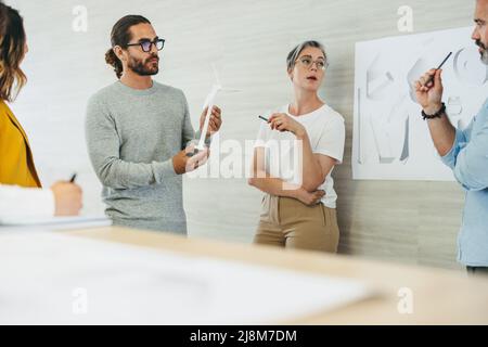 Creative design professionals having a discussion while working with wind turbine 3D models and drawings. Team of innovative businesspeople planning a Stock Photo