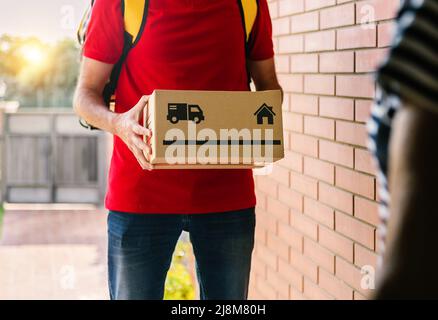 Close up of delivery man hands delivering cardboard box to customer at home entrance Stock Photo