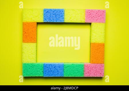 rectangular frame of multicolored sponges on yellow background, top view Stock Photo