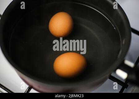 Two boiled brown eggs in a pot of boiling water Stock Photo
