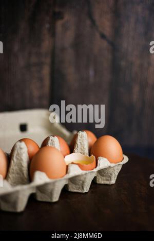 Fresh brown eggs and a broken egg with yolk in an eco tray made from recycled paper on a dark wooden background Stock Photo
