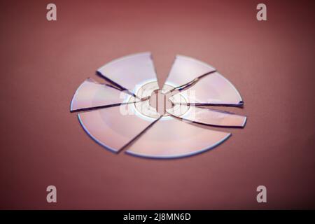 Broken compact disc divided into parts close-up on a red-burgundy background, complete loss of data Stock Photo