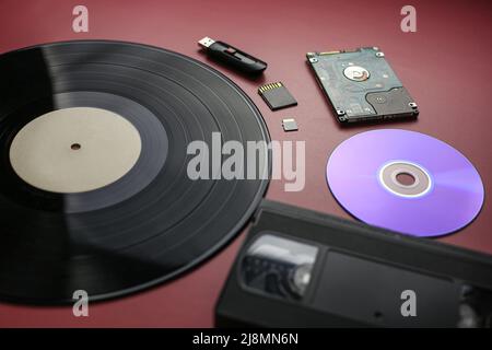 The evolution of recording and storing music and data, vinyl record, cassette, disk, hard drive, flash cards on a red-burgundy background, close-up Stock Photo