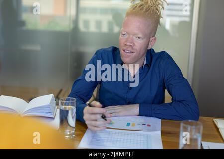 African american mid adult albino businessman looking away while working on graphs at desk in office Stock Photo