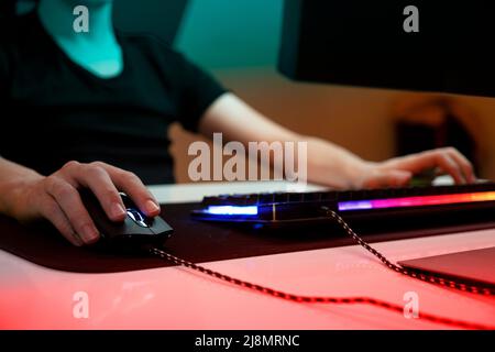Hands on mouse, selective focus to young gamers hands on mouse. At night, alone in his dark room with warm neon lights. Stock Photo
