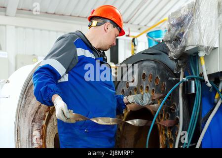 Engineer in helmet inspects and repairs gas equipment of boiler room. Cleaning and maintenance of industrial steam boiler. Stock Photo