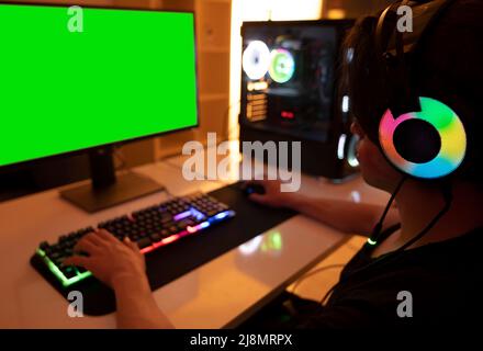 Playing on computer, teenage gamer boy playing on computer in his room at night. Room and computer has warm neon lights. Stock Photo