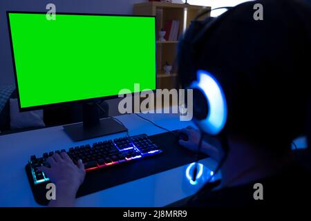 Blurred green computer screen, selective focus on teenage who is using computer in a dark room. Teenage wearing a headset with a mic. Stock Photo