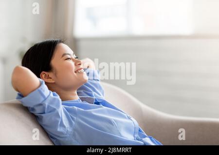 Cute chinese woman resting on sofa at home, copy space Stock Photo