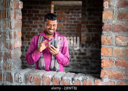 Happy smiling young indian labour busy on mobile phone at workplace - concept of using social media application, technology and leisure activity. Stock Photo