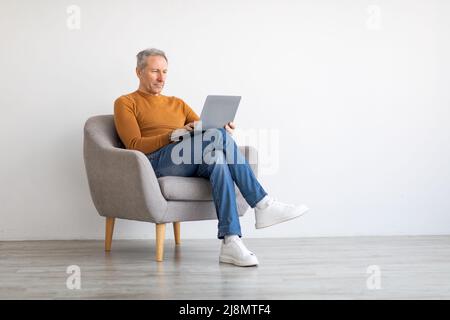 Confident mature man using laptop sitting on chair Stock Photo