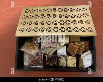 A partially opened gift box of Indian mixed sweets, placed on a brown wooden table. Stock Photo