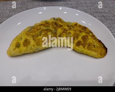 Freshly cooked Egg omelette stuffed with cheese, vegetables and ham, served on a white plate and placed on a table with textured fabric below. Stock Photo