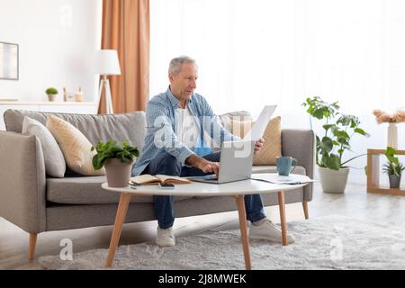 Man holding documents reading report working on laptop at home Stock Photo