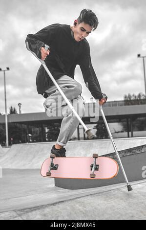 Guy on crutches in air jumping on skateboard Stock Photo