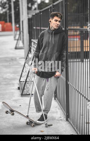 Guy on crutches standing near skateboard in park Stock Photo