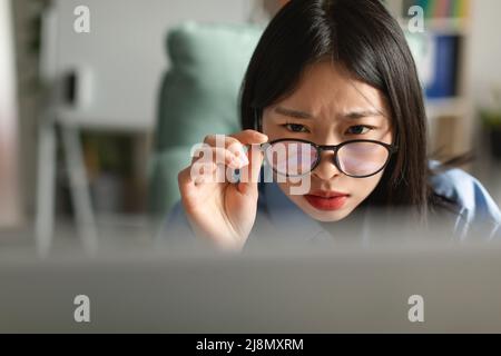 Confused Asian lady using laptop looking at screen Stock Photo