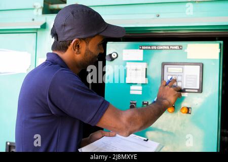 Electrical engineer noting down voltage flow of switch gear or current distribution board at industrial company - concept of blue collar job Stock Photo