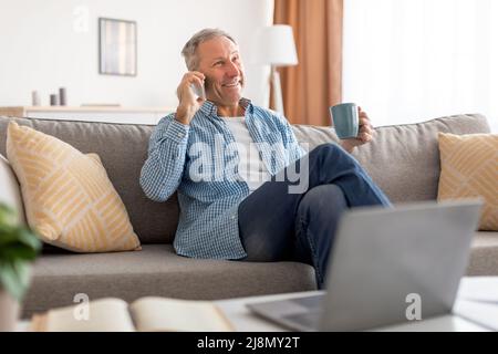Cheerful mature man talking on cellphone sitting on sofa Stock Photo