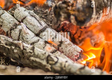 A close-up shot of pieces of logs and firewood, charcoal and ashes burning in flames. Stock Photo