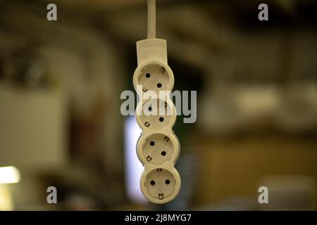 Electrical outlet hangs on wire. Extension cord for current. Four plug inputs. Stock Photo