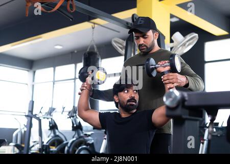 Gym trainer helping athlete to use dumbells during workout - concept of fitness training, personal coach and bodybuilding. Stock Photo