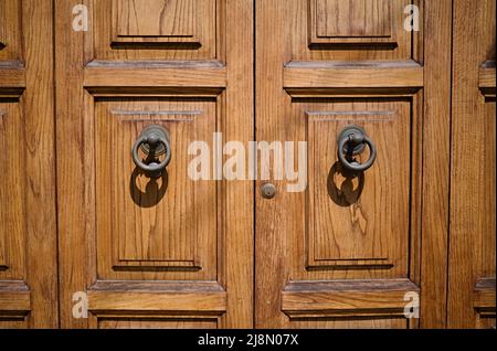 Massive wooden entrance doors with round metal handles and small keyhole close up. Double doors in solid wood in natural wooden color Stock Photo