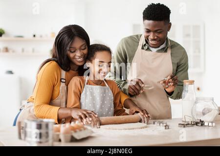 Cheerful Black Family Baking Pastry Rolling Out Dough In Kitchen Stock Photo