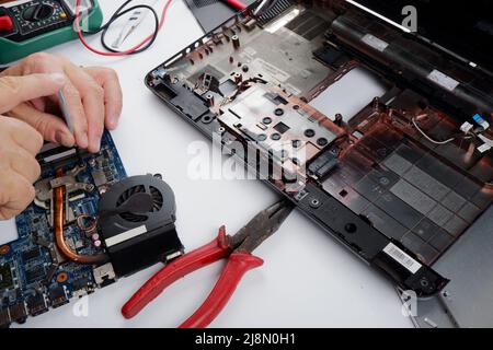 a computer repairman disassembles, repairs and does preventive maintenance for a broken laptop. Stock Photo