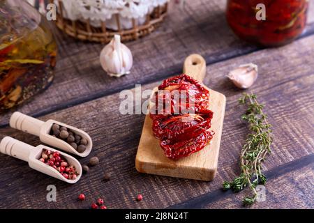 Sun-dried tomatoes in olive oil on a mini board with pepper, garlic and thyme in a rustic style. Selective focus, close-up. Stock Photo