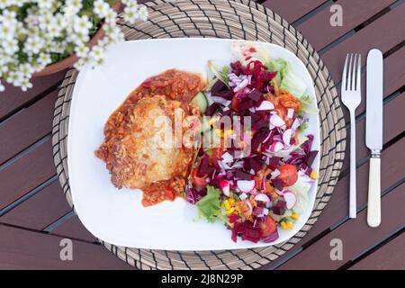 A Mary Berry meal recipe called Mexican Bake, served with a salad and placed on a garden table. Made with Tortilla wraps, mincemeat and cheese Stock Photo