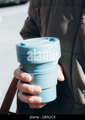 Female hands hold blue reusable coffee mug. Sustainable lifestyle. Eco friendly concept. Stock Photo