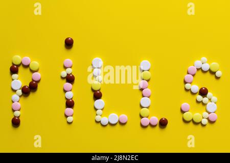 top view of pills word made of colorful round shape medication on yellow background Stock Photo