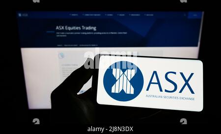 Person holding smartphone with logo of Australian Securities Exchange Ltd (ASX) on screen in front of website. Focus on phone display. Stock Photo