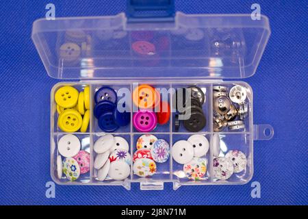 Small buttons for clothes of different types lie in the cells of a plastic container. Stock Photo