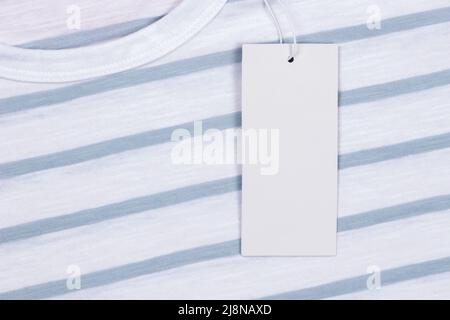 Blank white rectangular label tag on white striped t-shirt clothes background. Price tag tabel mock up with copy space Stock Photo
