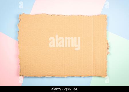 Piece of brown corrugated cardboard on colorful background. Ripped kraft carton paper card. Cardboard torn edge. Top view, copy space Stock Photo