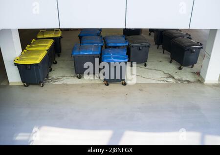 Many plastic garbage containers stand near the building, on the city street. Top view. Stock Photo