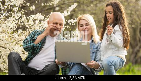 Happy different generations affectionate family having fun indoors, looking at laptop screen, enjoying watching funny comedian movie or recollecting Stock Photo