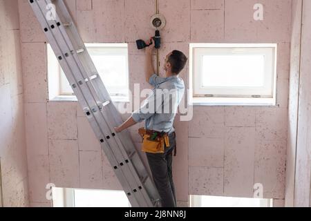An electrician fixing wires, installing light on the ceiling Stock Photo