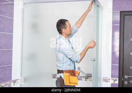 Young plumber man with tools repairing fixing faucet in shower stall. Stock Photo