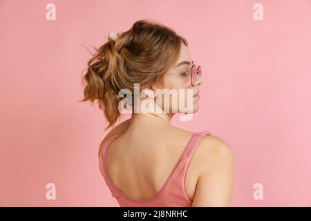Monochrome portrait of young attractive woman in crop top isolated on pink background. Concept of beauty, art, fashion, youth. Back view Stock Photo