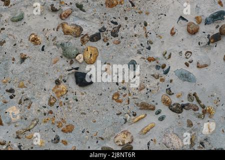 Texture of concrete with multicolored pebbles on the surface. Monolithic concrete wall or garden path with inclusion of multicolored pebbles. Stock Photo