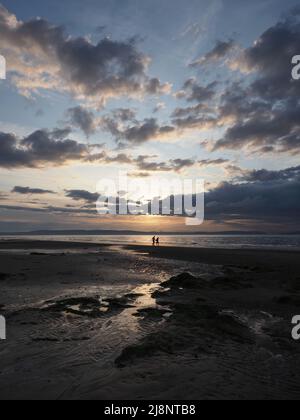 A couple walking hand in hand on Nairn Beach at low tide, on a summers evening as the sun goes down. Dramatic cloudscape. Stock Photo